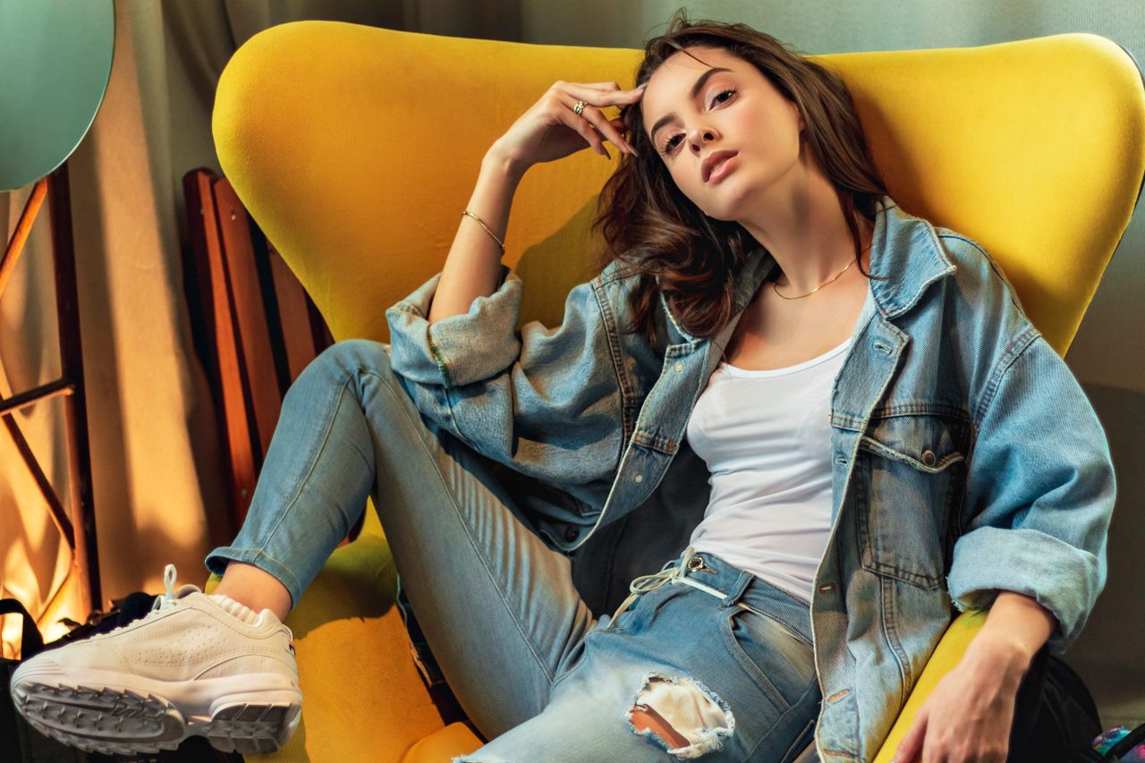 services-03 Stylish woman in denim poses on a modern yellow chair indoors.