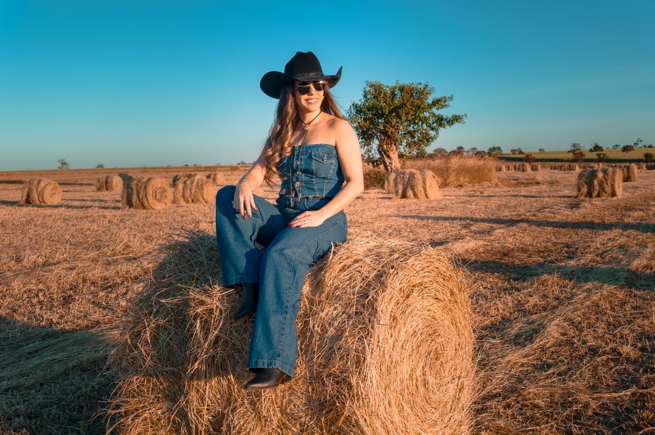 Mastering the First Impression: Your intriguing post title goes here Elegant woman in denim with cowboy hat and sunglasses sitting on a hay bale in a rural field.