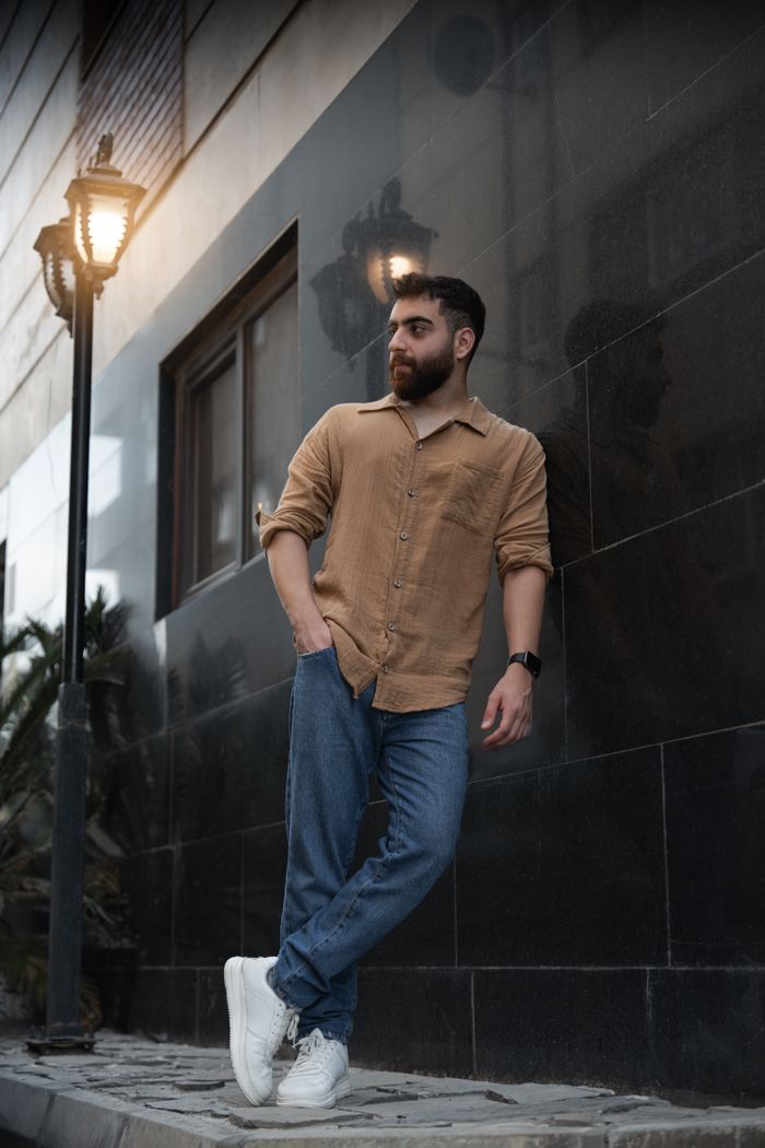 about-us Trendy young man with a beard leaning against a wall in a city street during evening time.