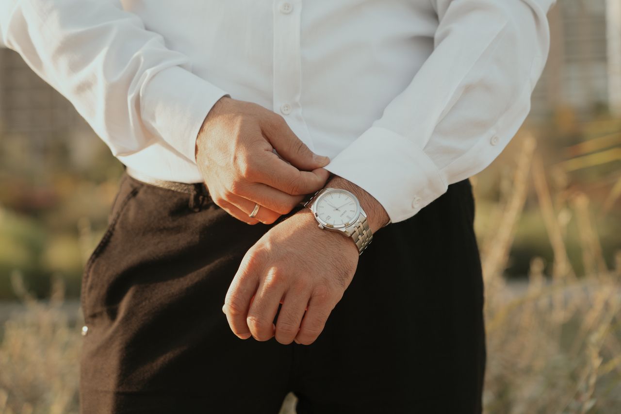 services-01 Close-up of a man adjusting a silver wristwatch outdoors in natural light.