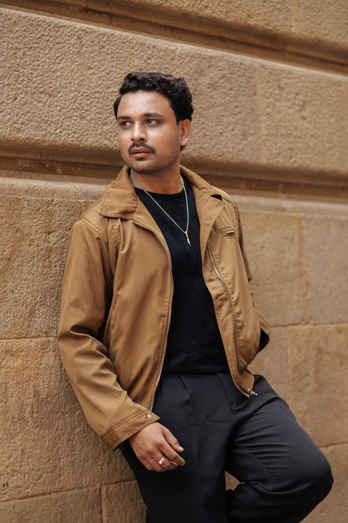 who-we-are Casual urban fashion with a man leaning on a brick wall wearing a jacket.